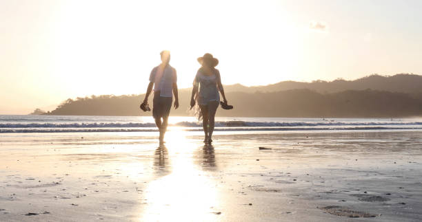 istock Mature couple walks down sandy beach at sunrise 1302832921