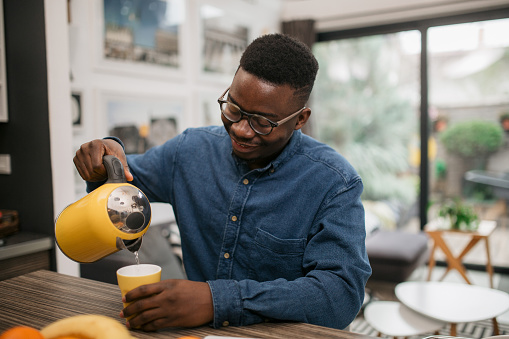 Handsome African American man preparing himself a cup of tea at home, smiling
