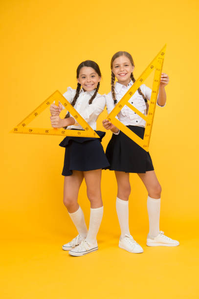istock geometric shapes. pupils use gon ruler. stem disciplines. back to school. Maths and geometry. Kids in uniform at yellow wall. friendship and sisterhood. happy small girls study mathematics 1302836049