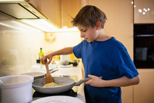 istock Little boy helping making crepes pancakes in kitchen 1302836136