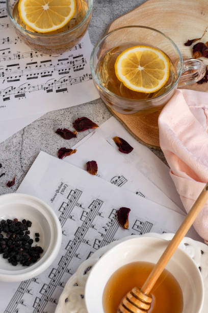 Cup of lemon tea and honey on grey background with music note sheets