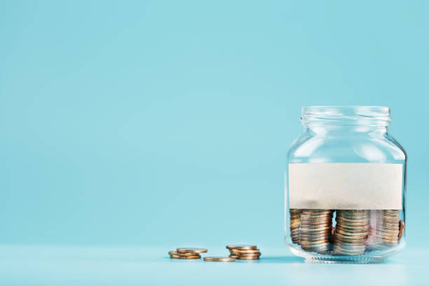 istock Glass jar with coins, with a sticker with free space for text, on a blue background. 1302842295