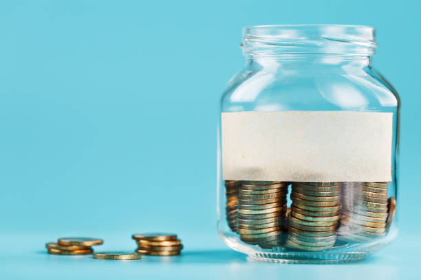 istock Glass jar with coins, with a sticker with free space for text, on a blue background. 1302842529