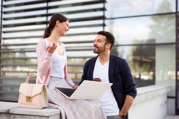 istock Smiling young woman talking to her colleague while using a laptop 1302844687