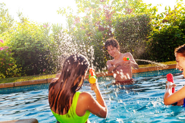 Teenagers friends play with water-gun in pool Group of three teens play with water-gun squirt pistol on swimming pool outside on sunny day squirting stock pictures, royalty-free photos & images