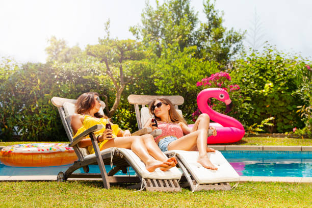 istock Two girls friends talk, relax on pool deck chair 1302848610