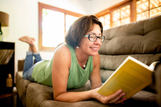 istock Smiling mature woman lying on her sofa reading a book 1302849174