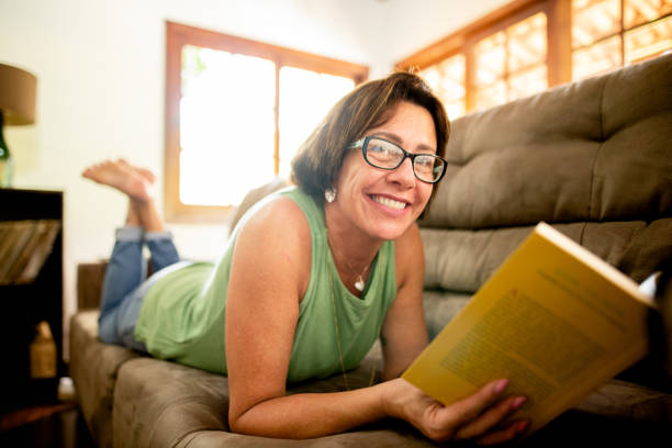 istock Smiling mature woman reading a book while lying on her sofa 1302849211