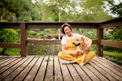Smiling mature woman sitting with her dog outside on a wooden patio in her back yard