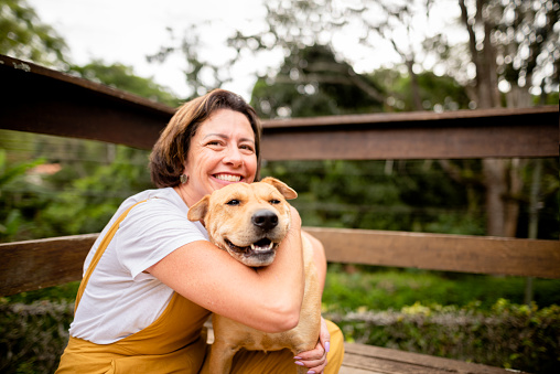 Mujer madura sonriente abrazando a su perro afuera en su patio photo