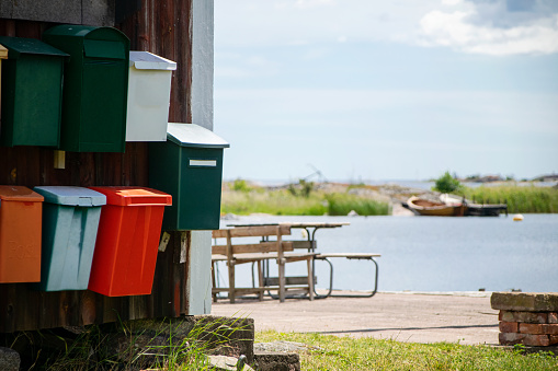 Mailboxes in different colors on wooden house exterior outdoors in the Swedish archipelago with the sea view in the background on a summer day in Sweden.
