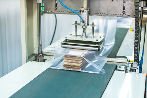 wood flooring planks being covered in plastic protection with factory machine