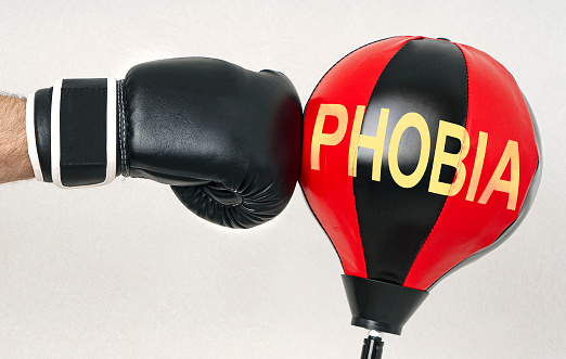 Fight the phobia concept with a strong man's hand in a boxing glove hits the punching bag with text Phobia.