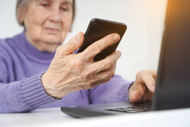 istock An elderly woman makes an order and payment online. She holds a smartphone in one hand, while the other is typing on the computer. 1302865717