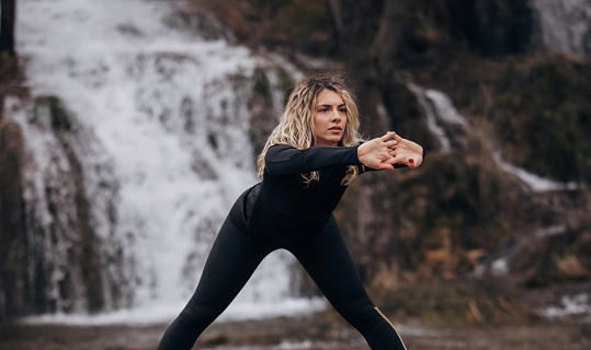 One woman, beautiful fit young woman exercising alone by the waterfall in nature.