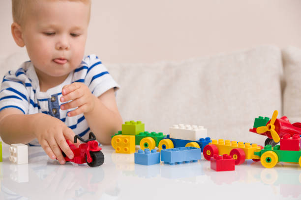 istock Child playing with colorful plastic bricks at the table. Toddler having fun and building out of bright constructor bricks. Early learning.  stripe background. Developing toys 1302869088