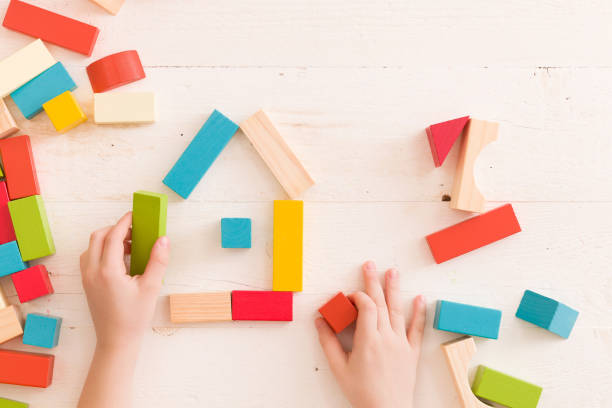istock Top view on child's hands playing with colorful wooden bricks on the white table background.Kid building with geometric shapes. Learning and education concept. 1302869695