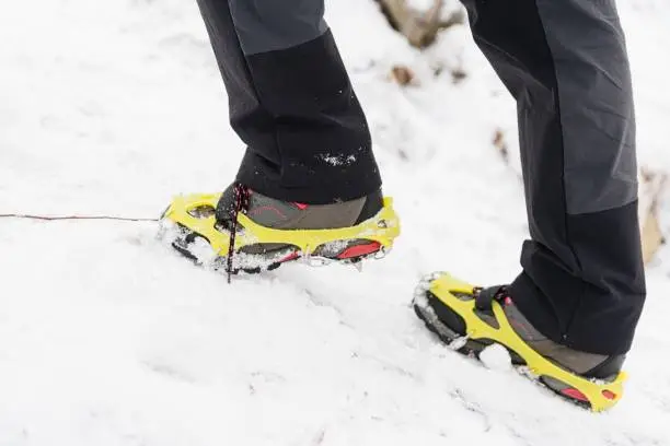 Tourist woman hiking in the snowy mountains. Yellow crampons on shoes.