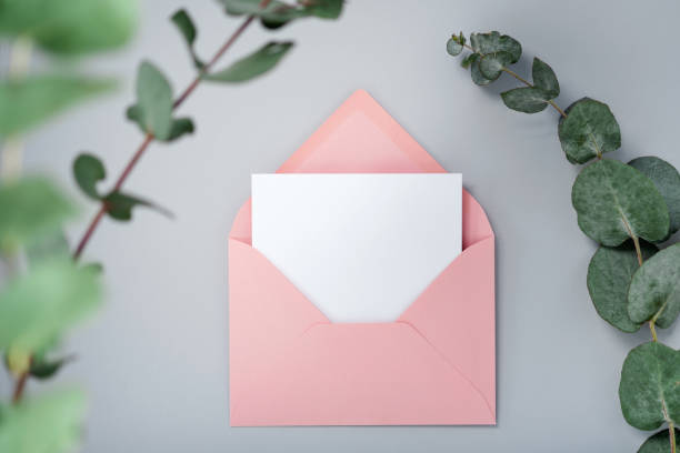 istock Real photo. Pink envelope square invitation card mockup with a eucalyptus branch. Top view with copy space, light gray background. Template for branding and advertising 1302872409