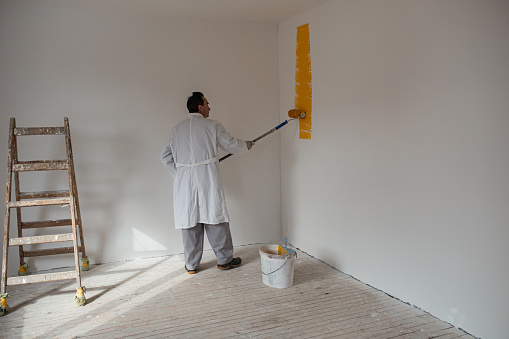 Man in white coat painting wall in yellow