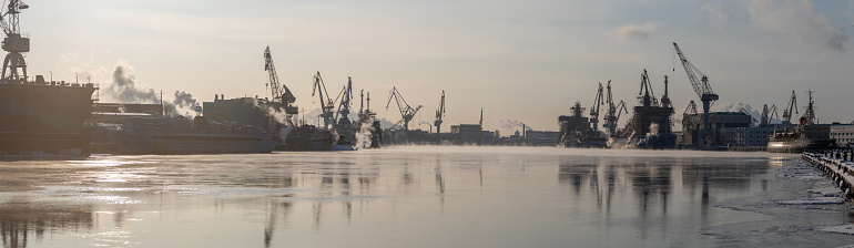 Cranes of of the Baltic shipyard on a frosty winter day, steam over the Neva river, smooth surface of the river, mirror reflection on the water, ships under construction, trawlers, nuclear icebreakers. High quality photo