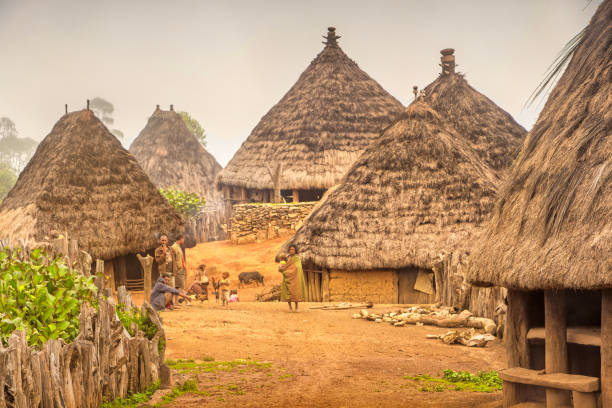 People socialize at the hilltop village of Nermelau in East Timor, with hatched roof mud huts in the background.