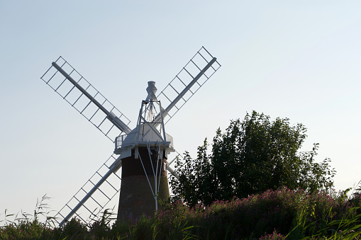 A rear view of a windmill (wind pump): tall traditional countryside building, surrounded by trees and bushes