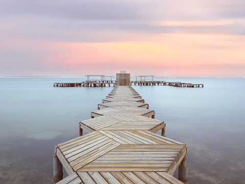 Wiew of a wooden pier in Mar Menor lagoon, from Los Alcazares, Murcia, Spain at dawn. A long boardwalk on the calm water of the lake at dusk.