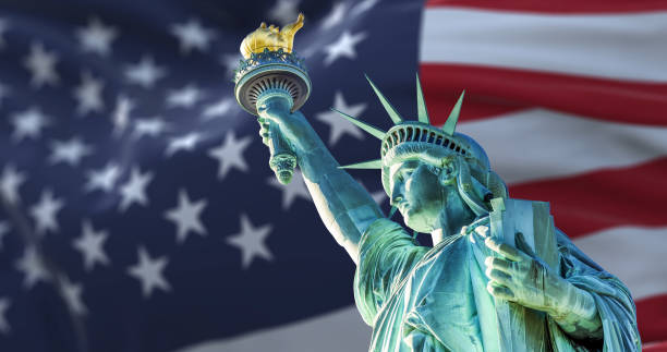the statue of liberty with the blurry american flag waving in the background - estátua da liberdade imagens e fotografias de stock