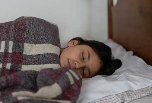 Portrait of a Latin American girl living at a rural house and sleeping in her bed covering with a rustic blanket - lifestyle concepts