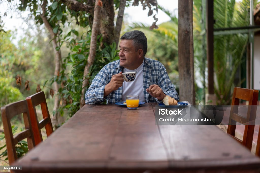 Adult man at a farm having breakfast at an outdoors dining room Adult Latin American man at a farm having breakfast at an outdoors dining room and drinking a cup of Colombian coffee Coffee Crop Stock Photo