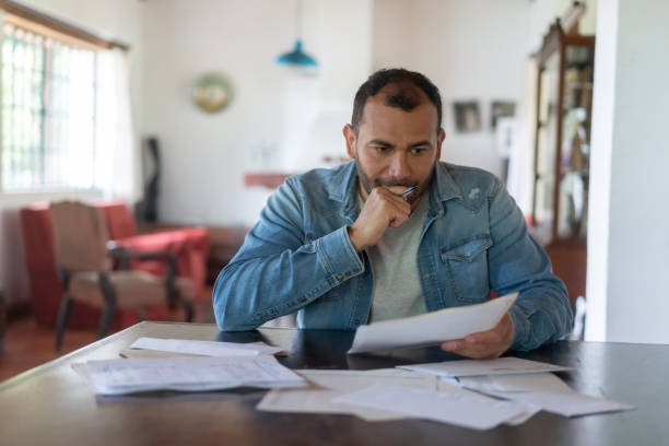 homme à faible revenu vérifiant ses finances à la maison et regardant inquiété - banqueroute photos et images de collection