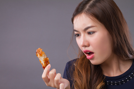 woman eating unhealthy fat fried chicken; portrait of unhealthy girl eating fat fried chicken, fast food; unhealthy eating, dining with high cholesterol fat concept; asian chinese 20s woman model