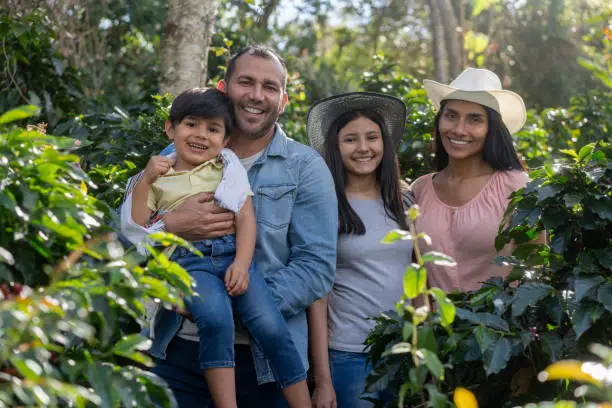 Happy family of Colombian coffee farmers working at a plantation and looking at the camera smiling