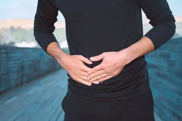Photo of Man in black sports clothes suffering from stomach side stitch or cramps during running. Side pain after jogging.