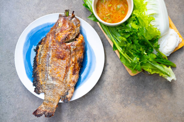 ปลานิลย่างเกลือในอาหารไทยกินกับซอสทะเลและผักสดเป็นอาหารไทยที่ดีต่อสุขภาพ - ปลา ภาพสต็อก ภาพถ่ายและรูปภาพปลอดค่าลิขสิทธิ์