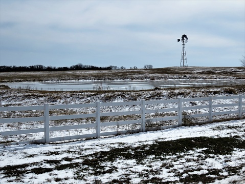 A stark barren snow landscape with a frozen cow pond and windmill in the distance in Texas on February  2021. Copy Space.