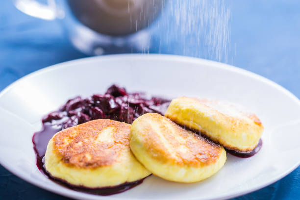 frühstück und leckeres konzept - pfannkuchen aus hüttenkäse mit marmelade, blauem hintergrund. mit puderzucker bestreuen. - cheesecake syrup cottage cheese cream stock-fotos und bilder