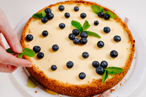 homemade cheesecake hand decorating with blueberry berries and mint leaves. Cooking desserts and cakes. Confectionery.
