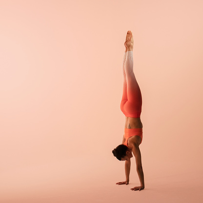 Mujer atlética con ropa deportiva, pantalones y top, realizando handstand en yoga photo