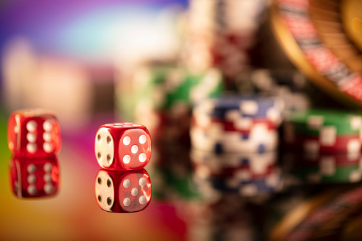 Roulette, dice and poker chips on a colorful bokeh background.
