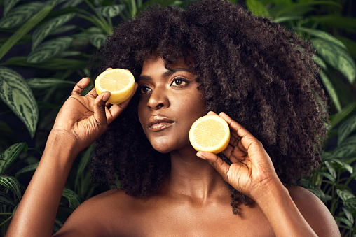 Shot of a beautiful young woman holding juicy lemon halves against a leafy background