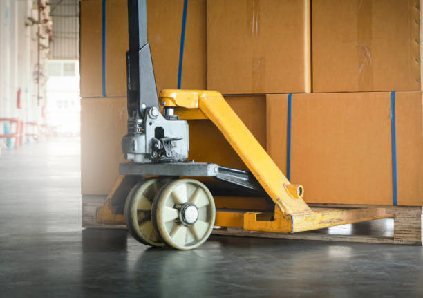 istock Close-up, Yellow hand pallet truck with cardboard boxes stack on pallet rack. 1302918234