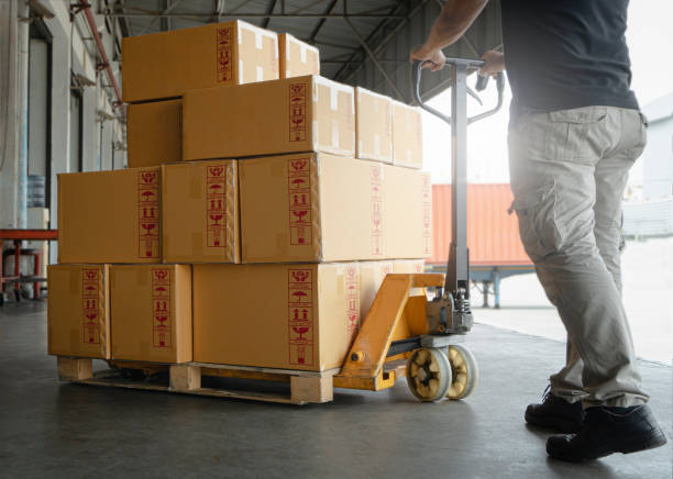 istock Woker working with hand pallet truck. worker unloading cardboard boxes stack on pallet rack. Shipment boxes. Cargo warehousing. 1302918239