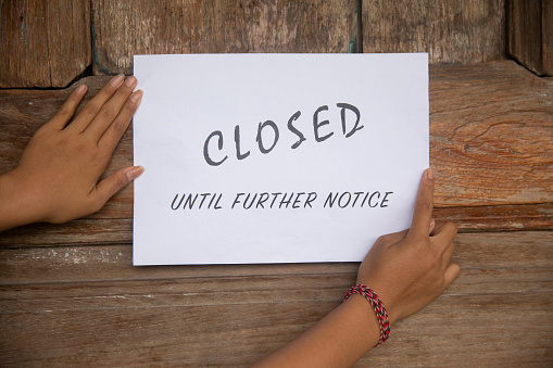 Close up shot of female hands putting a closed sign business on the wooden door during Covid 19 pandemic