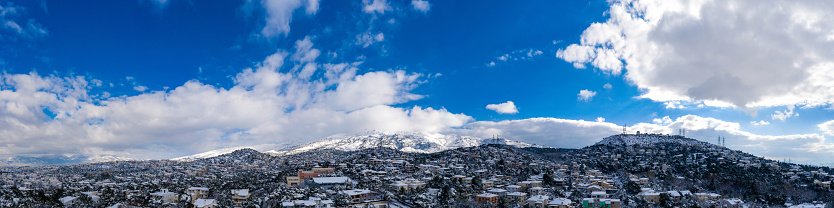 Attica Greece. Penteli mountain peak covered with snow. Snowy landscape panoramic view, winter day. Aerial drone view, blue cloudy sky background