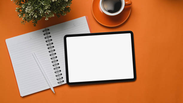 istock Mock up digital tablet with empty screen, notebook, coffee cup and plant on orange background. 1302921127