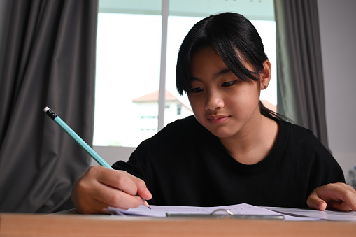 Asian children girl doing homework on wooden desk at home.