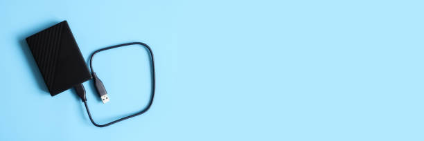 istock external hard drive black color with connection cable on blue background. banner 1302923136