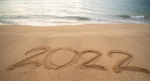 istock Handwriting year 2022 on sand and foam wave on beach. 1302924868